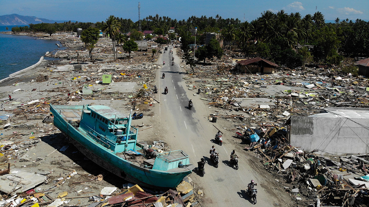 Le 1er octobre 2018, des personnes passent devant un bateau échoué et des bâtiments effondrés à Palu, après le tremblement de terre et le tsunami qui ont frappé la région le 28 septembre.
