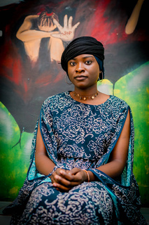 Awa pose devant une œuvre murale peinte pour sensibiliser aux violences sexuelles. © A. Faye / HI