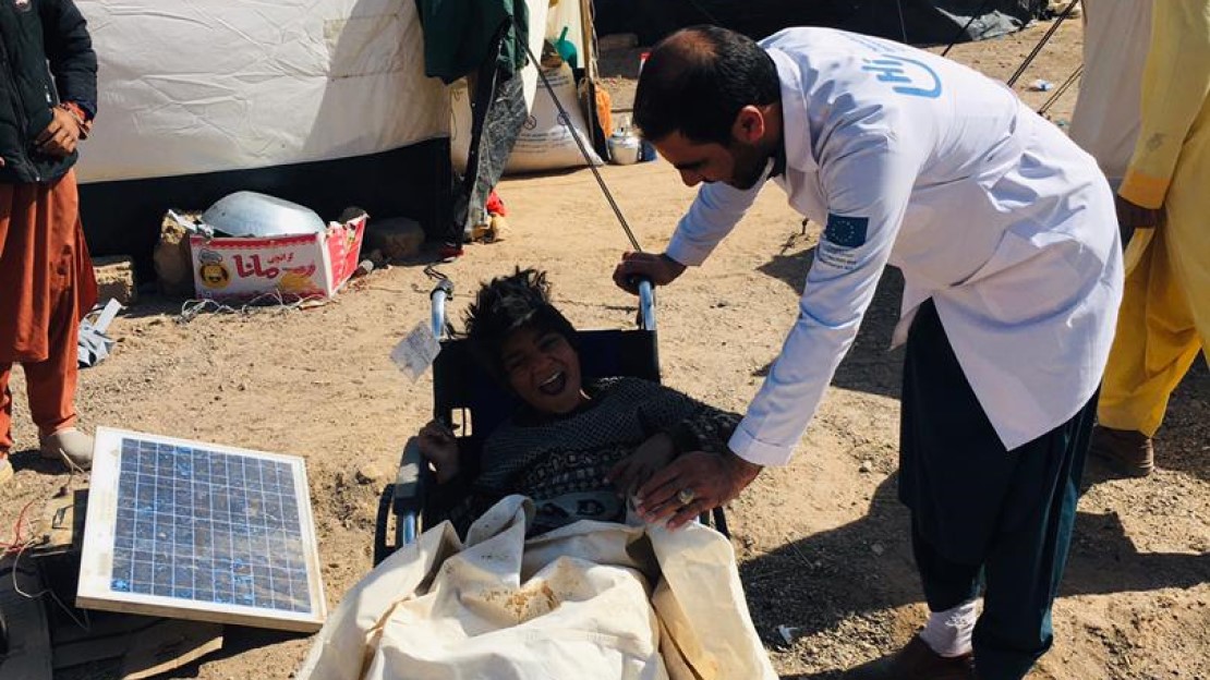 Un kiné HI se tient à côté d'un enfant en fauteuil près des abris. 
