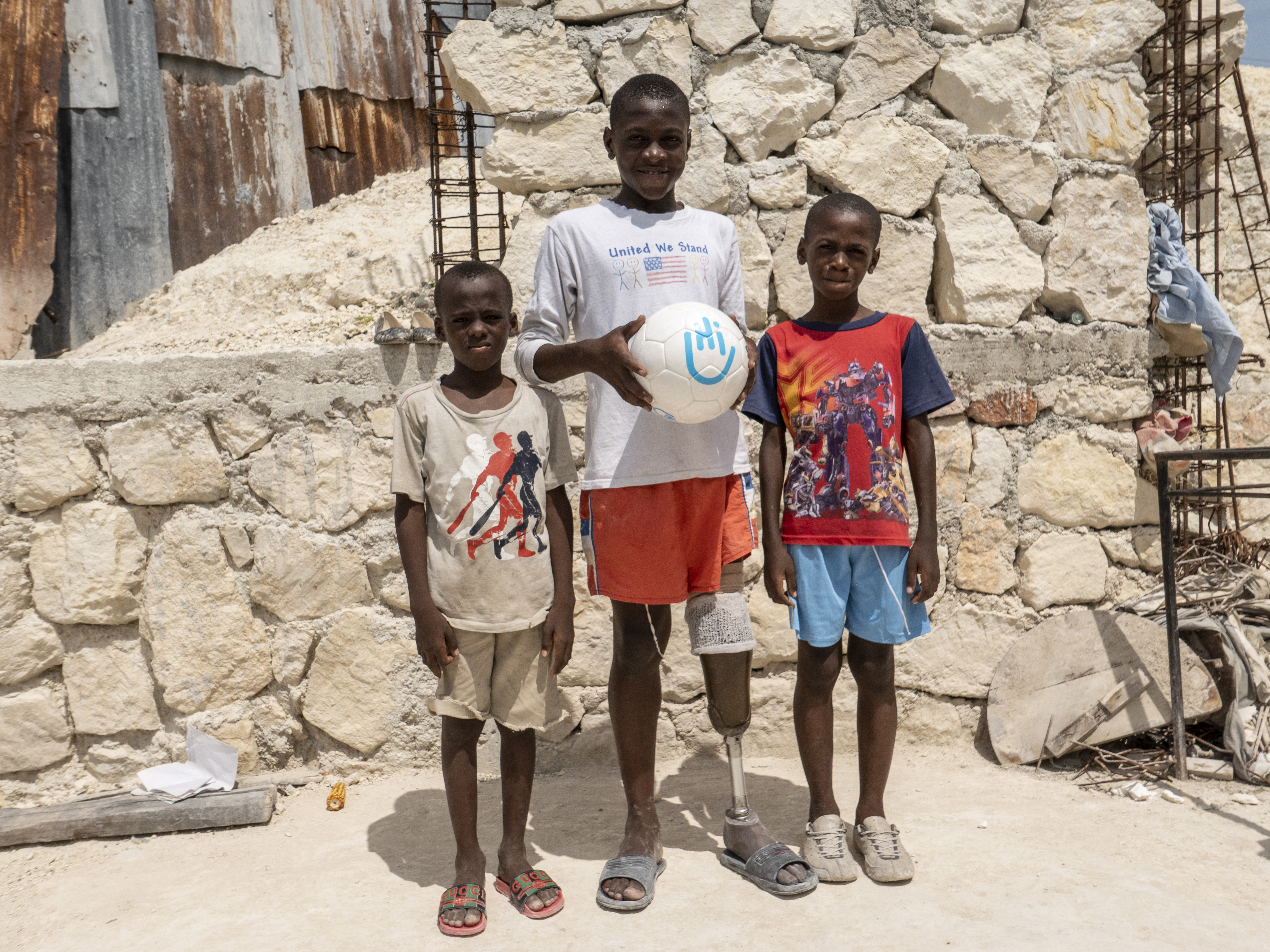Moise und seine Brüder. Moise hält einen Fußball mit HI-Logo. Er verlor sein linkes Bein durch das Erdbeben und kann heute mit Prohese wieder Fußball spielen.