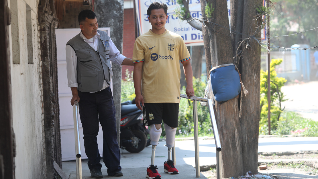 Un homme debout avec deux prothèses aux jambes se tenant à une rampe accompagné par un médecin.