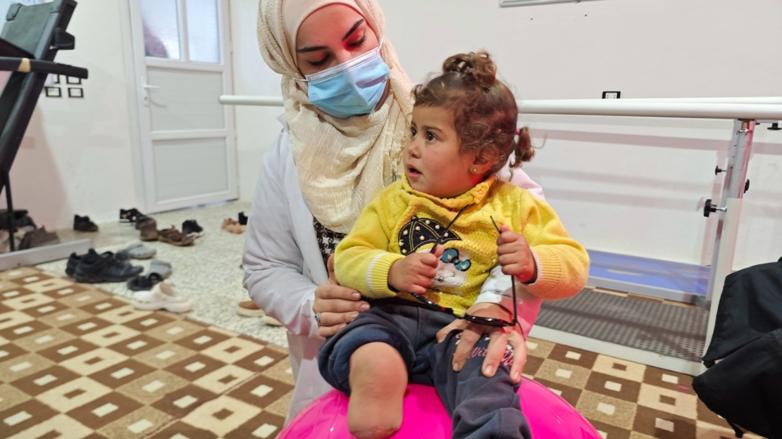 Noor, 3 ans, a été grièvement blessée pendant le séisme du 6 février 2023. Après sept mois d’hospitalisation, elle continue à être suivie régulièrement par les équipes de l’hôpital Aqrabat, partenaire de HI dans le Nord-Ouest de la Syrie. En photo ici avec sa kinésithérapeute.  